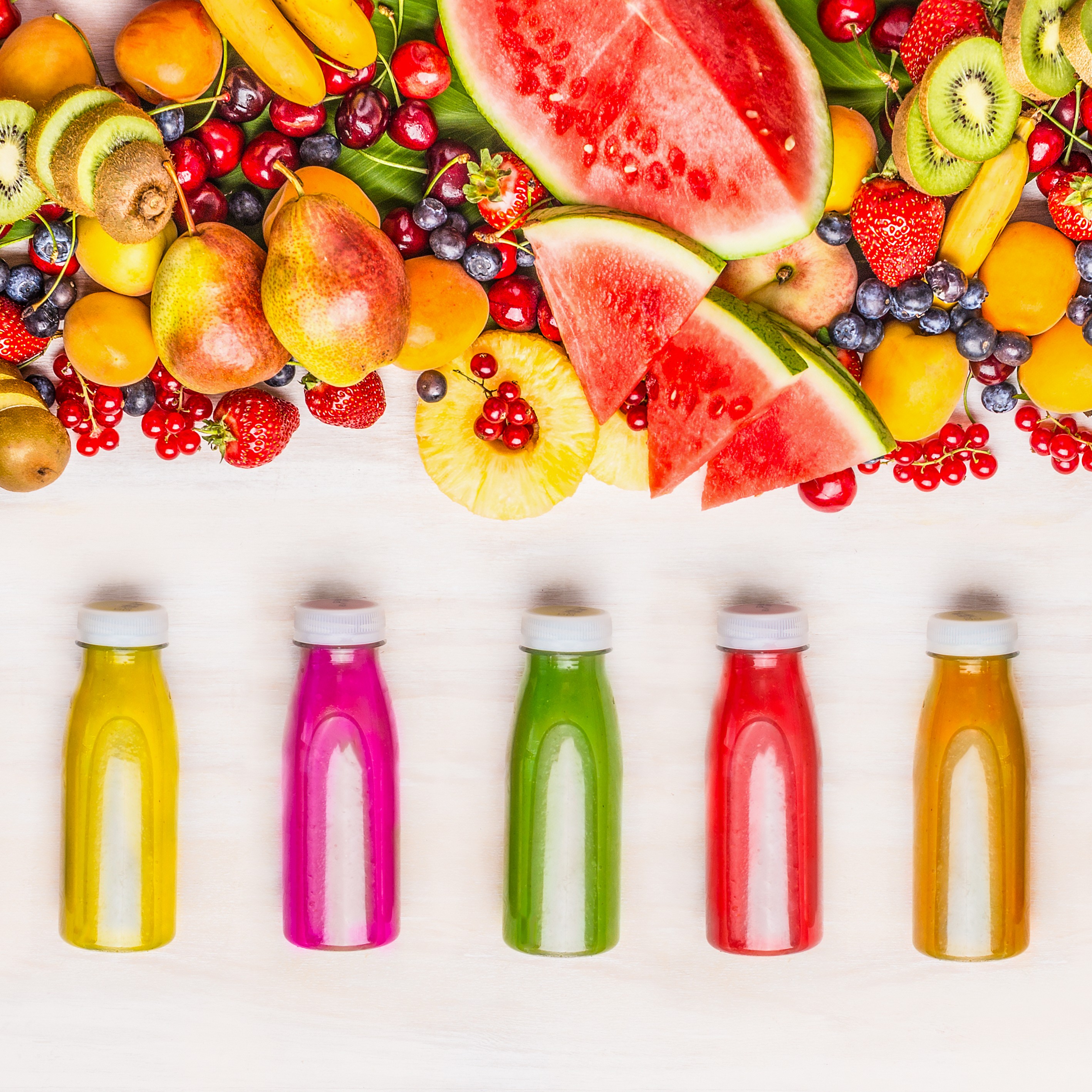 Varietà di frullati colorati e succhi di frutta in bottiglia con vari ingredienti freschi di frutta e bacche organiche su fondo di legno bianco, vista dall'alto.Concetto di cibo sano