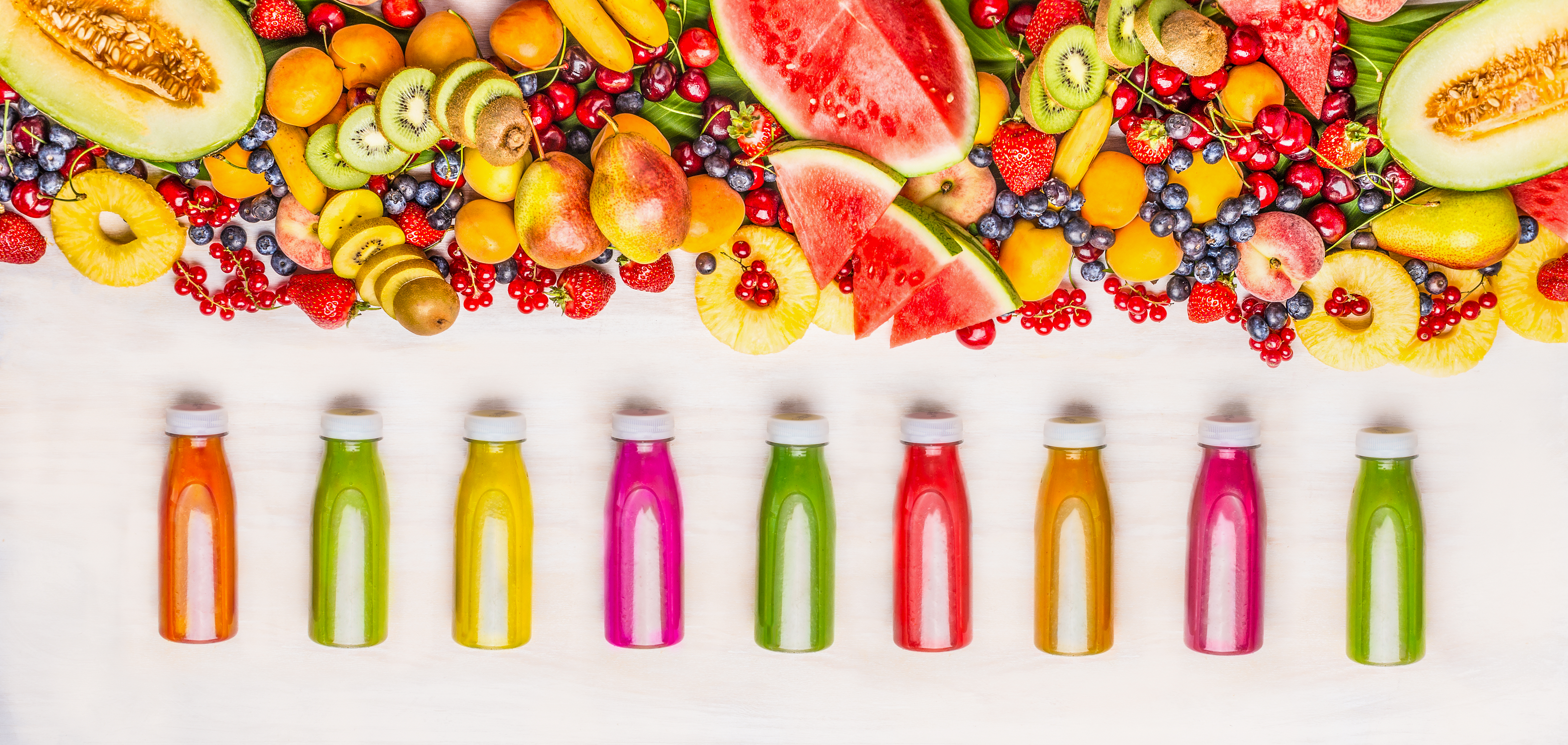 Разнообразие от цветни смутита и сокови напитки в бутилки с различни съставки от пресни органични плодове и горски плодове на бял дървен фон, изглед отгоре.Концепция за здравословна храна
